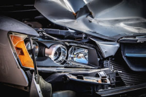 Closeup of a wrecked silver car with damage to the front headlight.