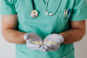 A male doctor wearing green scrubs holding a handful of pills in both palms