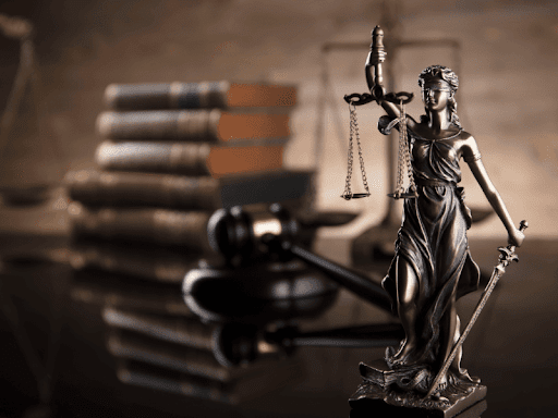 Close-up of a Lady Justice statue with a judge’s gavel and law books in the background 